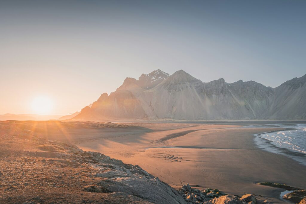 The sun is setting over a beach with mountains in the background